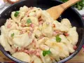 Pyszne kluski szklane z boczkiem i natką pietruszki w czarnej patelni, gotowe do podania.