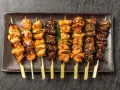 Różnorodne yakitori na talerzu: kurczak, warzywa i inne przysmaki, apetycznie wyglądające i gotowe do jedzenia.