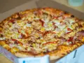 Pyszna, gorąca mrożona pizza w mikrofali, prosto z pudełka. Złocisty ser, kawałki ananasa i papryki kuszą apetycznie.