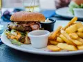 Pyszny burger z bekonem i frytki na talerzu. Idealny sposób, jak jeść burgera w restauracji, by delektować się każdym kęsem.