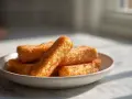 Złociste paluszki rybne z frytkownicy beztłuszczowej (airfryer) na talerzyku, kuszą chrupiącą panierką.