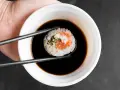 Pałeczki trzymają sushi z łososiem, zanurzając je w ciemnym sosie do sushi.