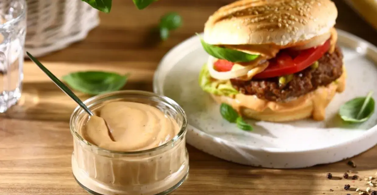 Pyszny sos do burgera w słoiczku, obok apetycznego burgera z dodatkami. Idealny do każdej kanapki.