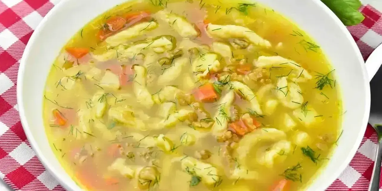 Aromaticzna zupa zacierkowa z kawałkami marchewki i świeżym koperkiem, podana w białej misce na czerwono-białej kratce.