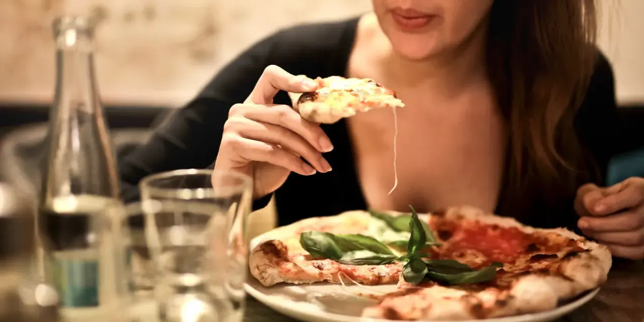 Smakowita pizza dla nas dwojga. Kobieta bierze kawałek, ciągnie się ser.