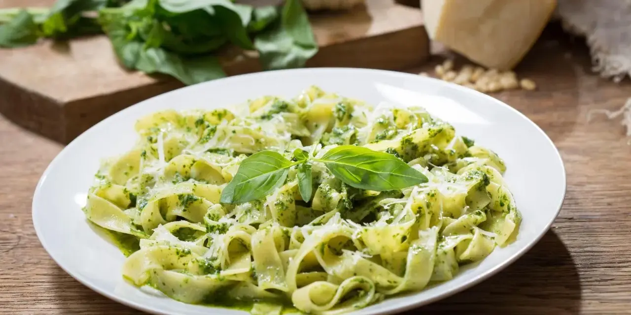 Talerz tagliatelle z aromatycznym pesto z rukoli, posypany parmezanem i udekorowany listkami bazylii.