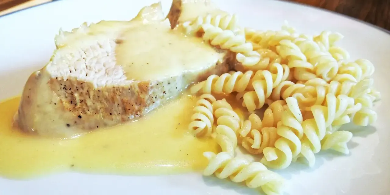 Kawałek pieczonego mięsa w kremowym sosie potrawkowym, podany z makaronem fusilli.