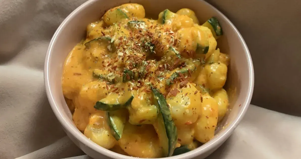 Puszyste gnocchi z cukinią w kremowym sosie, posypane ziołami i płatkami chili. Pyszne gnocchi z pesto w miseczce.
