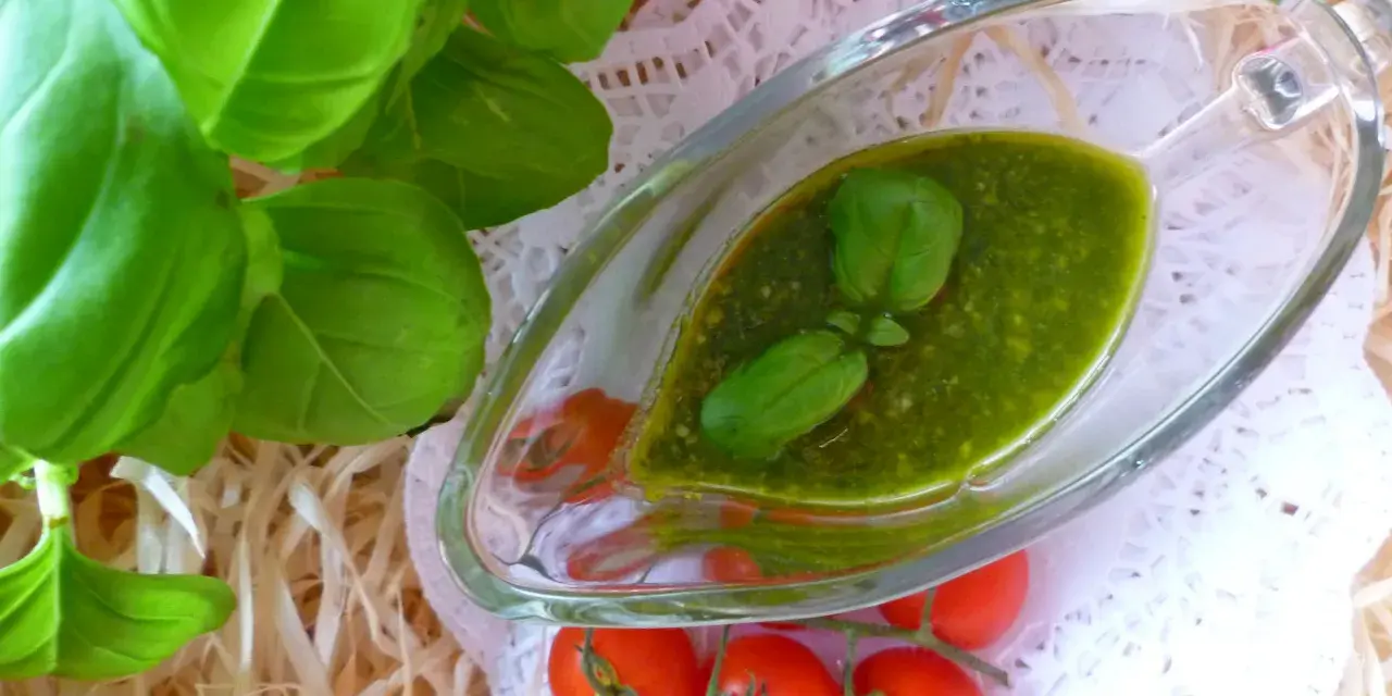 Świeże liście bazylii i pomidorki koktajlowe obok sosu pesto z bazylii w szklanym naczyniu.