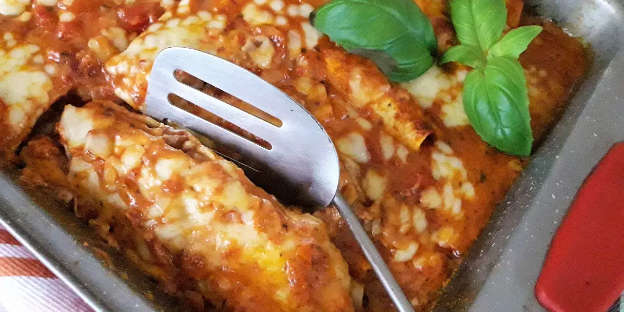 Zapiekana tortilla z mięsem mielonym, polana sosem pomidorowym i posypana serem, ozdobiona listkami bazylii.