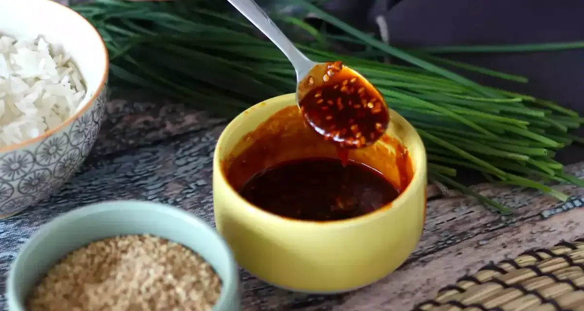 Łyżka z aromatycznym sosem gochujang, obok miseczki ryżu, sezamu i szczypiorku.