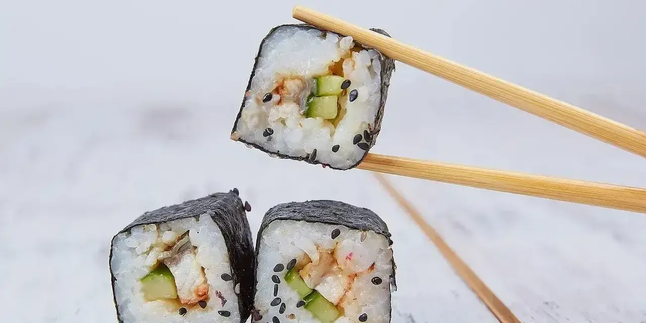 Trzy kawałki sushi z ryżem, ogórkiem i rybą, jeden podniesiony pałeczkami. Idealne do sosu, który stanowi zalewa do sushi.