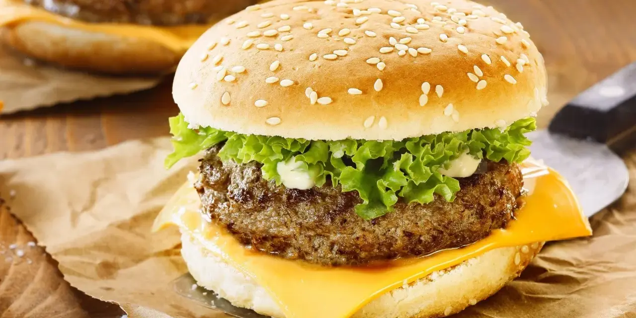 Zbliżenie na cheeseburgera z serem, sałatą i majonezem na bułce z sezamem.