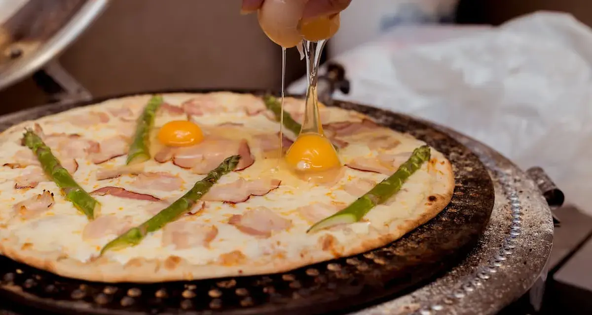 Ktoś dodaje jajko do pizzy z boczkiem i szparagami. Pyszna pizza z jajkiem w przygotowaniu.