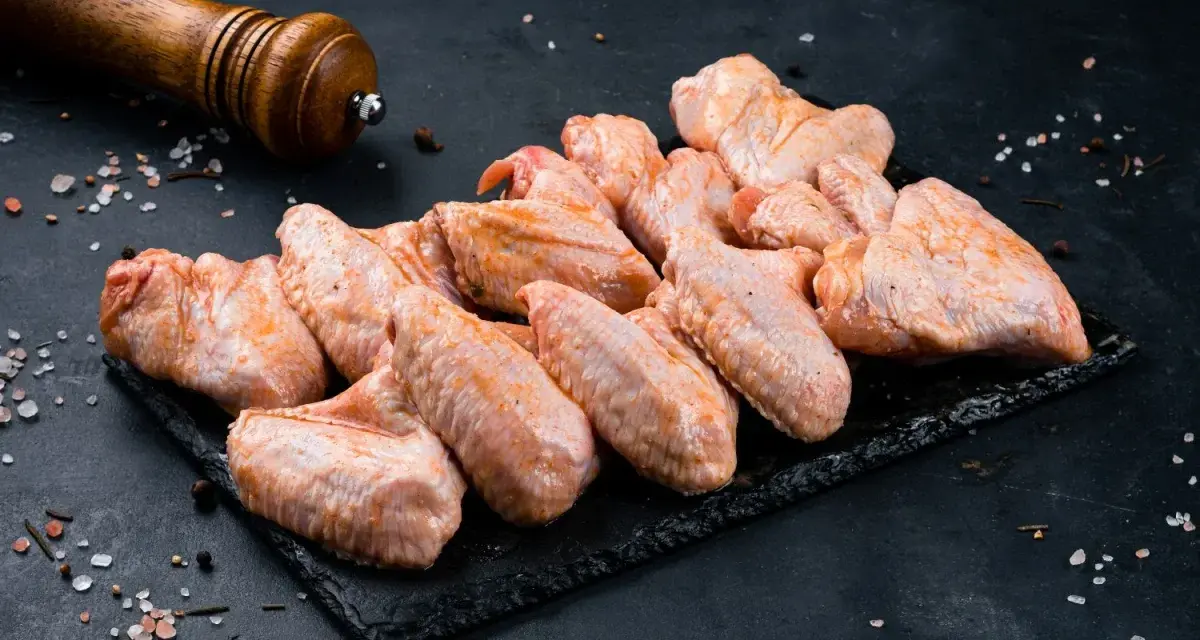 Skrzydełka kurczaka gotowe do pieczenia, zamarynowane w aromatycznej solance. Obok młynek do pieprzu i gruboziarnista sól.