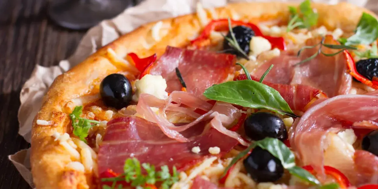 Pyszna pizza z cienko pokrojoną, aromatyczną szynką, czarnymi oliwkami i papryką. Idealna jaka szynka na pizzę!