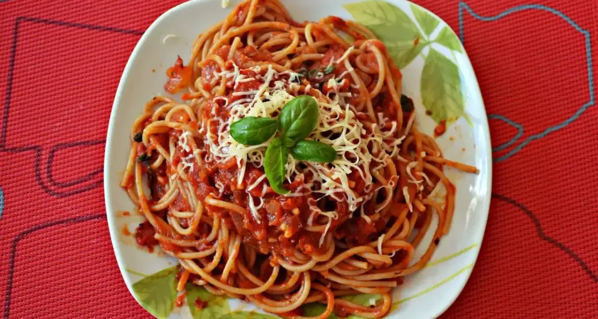 Pyszny sos do makaronu spaghetti z tartym serem i bazylią na talerzu.