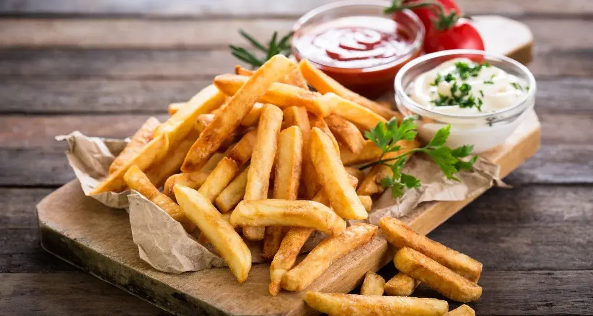 Złociste frytki na desce, idealne co do frytek na szybko. Obok ketchup i majonez.
