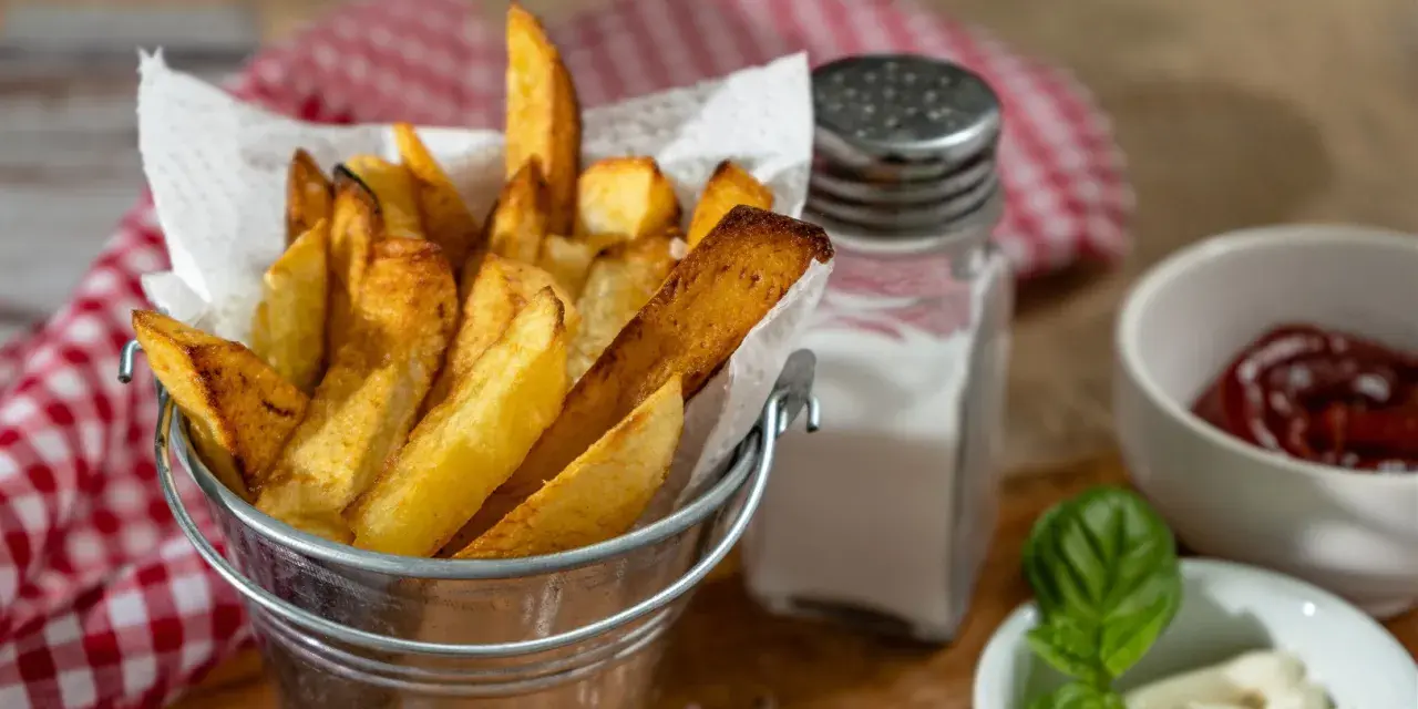Złociste frytki w metalowym wiaderku, obok solniczka i ketchup. Czy ziemniaki sałatkowe nadają się na frytki? Wyglądają pysznie!