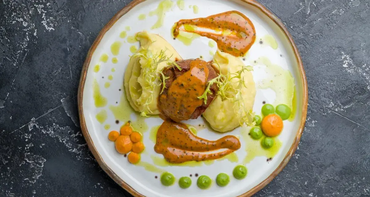 Mięso z puree ziemniaczanym, ozdobione pomarańczowym sosem do mielonych i zielonymi groszkami.