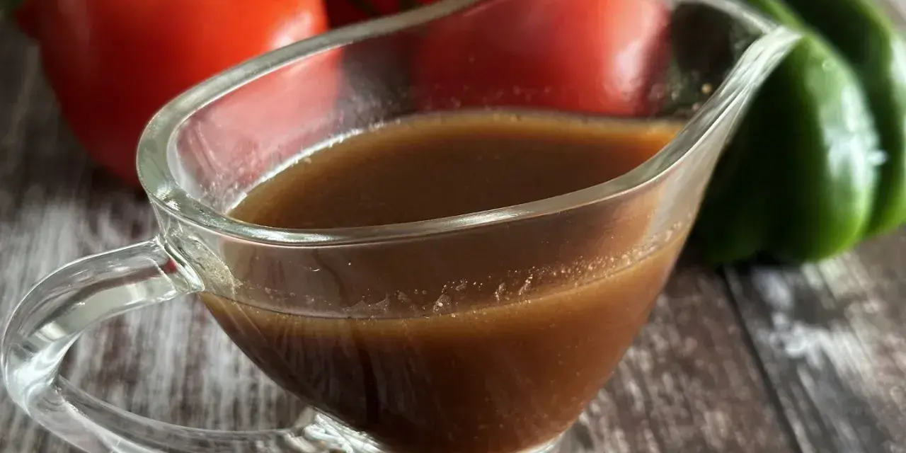 Sos balsamiczny w sosjerce, w tle pomidory i zielona papryka. Idealny do sałatek i mięs.