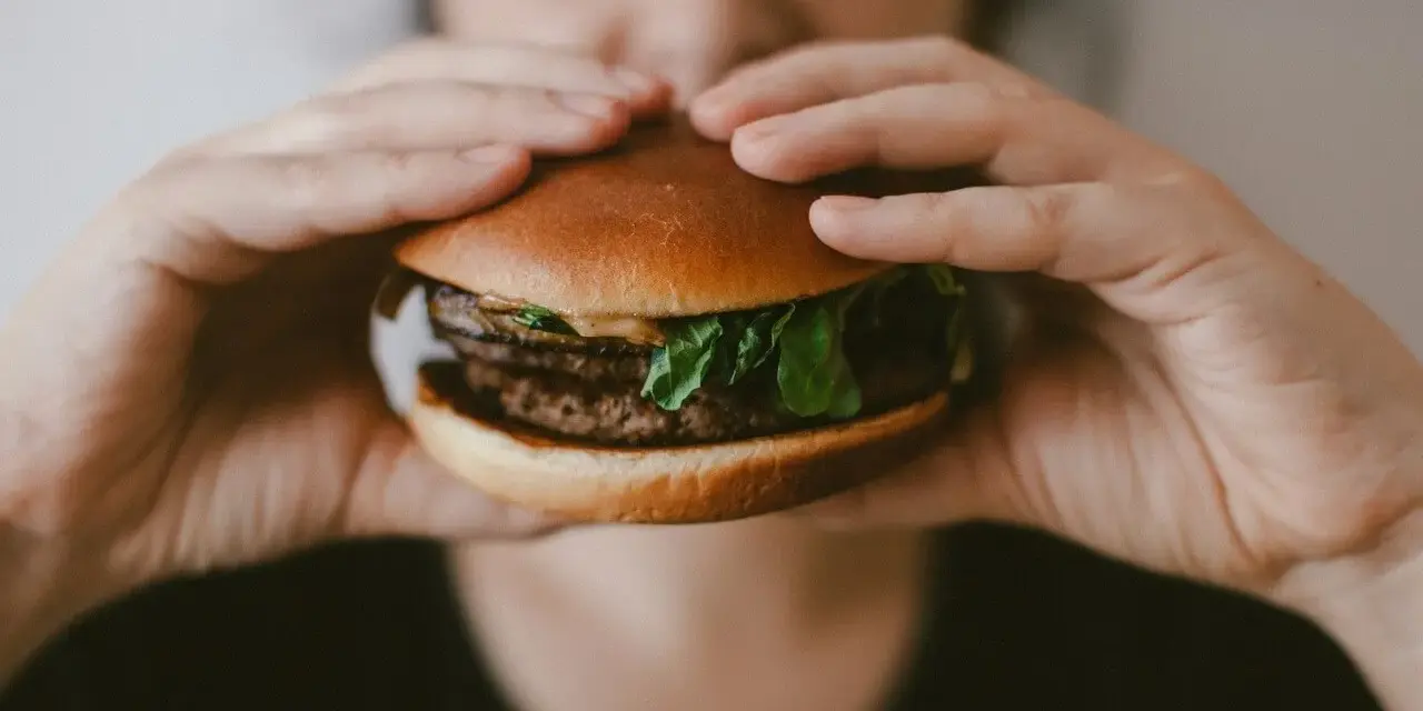 Osoba trzyma soczystego burgera, zastanawiając się, ile kalorii ma burger w restauracji.