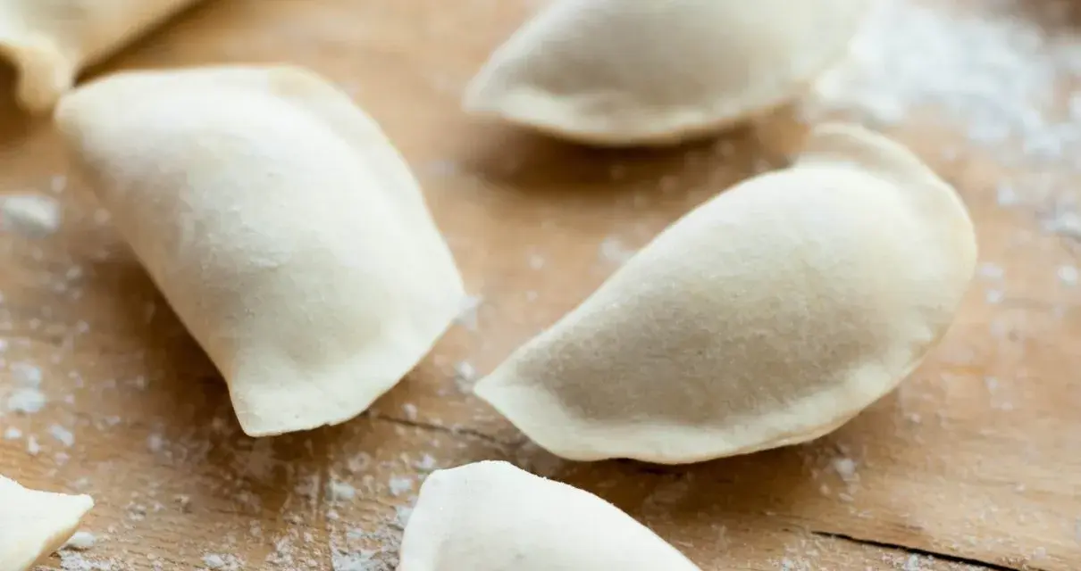 Surowe pierogi uformowane na drewnianej desce. To ciasto na pierogi bez jajka, gotowe do nadzienia.