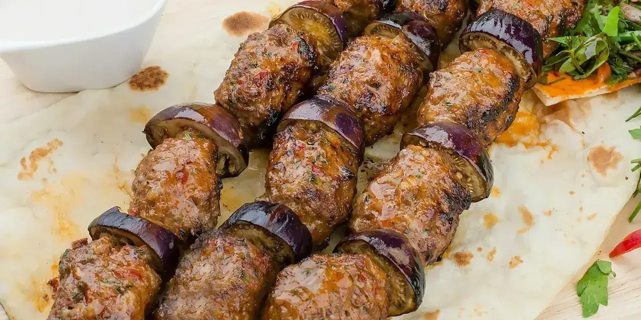 Kofta kebab z bakłażanem na płaskim chlebie, podany z sosem.