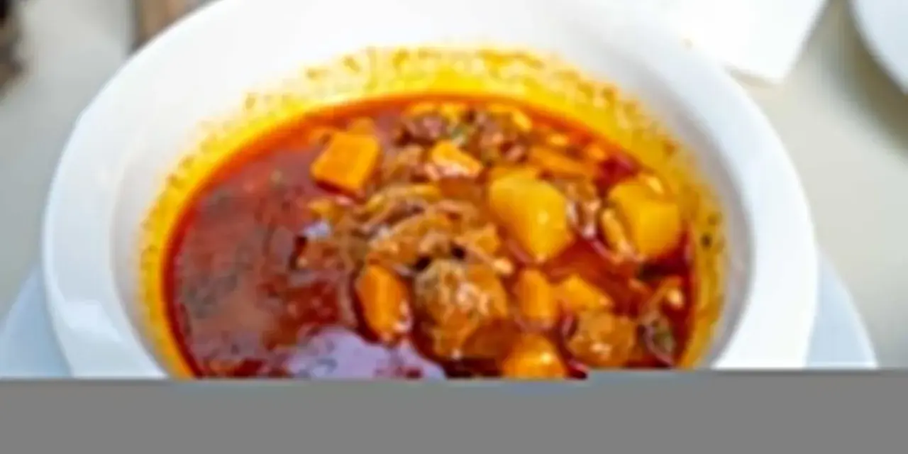 Zupa gulaszowa Ani gotuje się w głębokim talerzu. Mięso i ziemniaki w aromatycznym, czerwonym sosie.