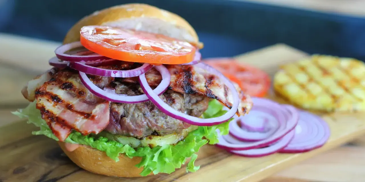 Soczysty burger z chrupiącym boczkiem, pomidorem, sałatą i czerwoną cebulą. Dodatki do burgera kuszą smakiem.