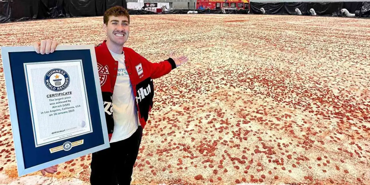 Mężczyzna prezentuje certyfikat Guinnessa za największą pizzę świata, która rozciąga się na ogromnej przestrzeni.