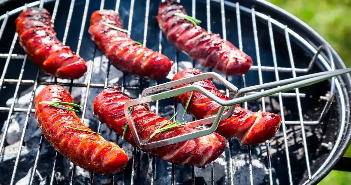 Aromatyczna kiełbasa z grilla, skwiercząca na węglu, z gałązkami rozmarynu. Idealna na letnie popołudnie.