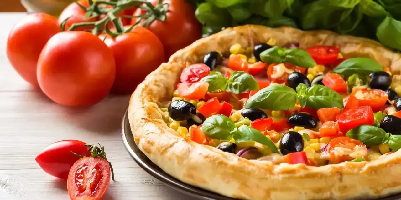Pyszna pizza z pomidorami, oliwkami i kukurydzą, obok świeże pomidory i bazylia. Ile piec pizze?