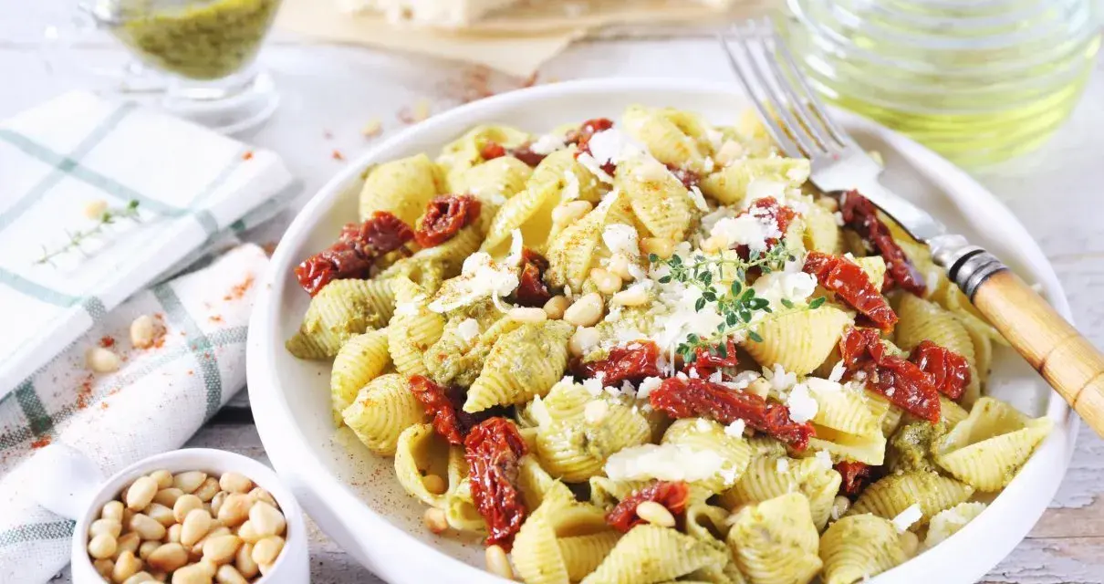Pyszny makaron z pesto i suszonymi pomidorami, posypany parmezanem i orzeszkami pinii.