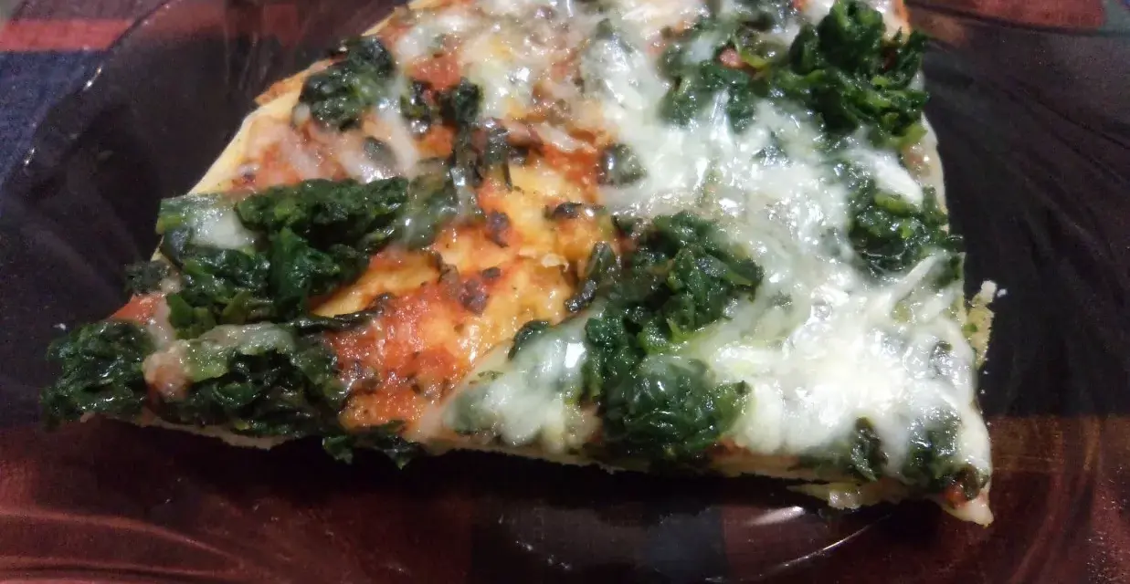 Kawałek pysznej pizzy ze szpinakiem, z ciągnącym się serem i pomidorowym sosem, na ciemnym talerzu.