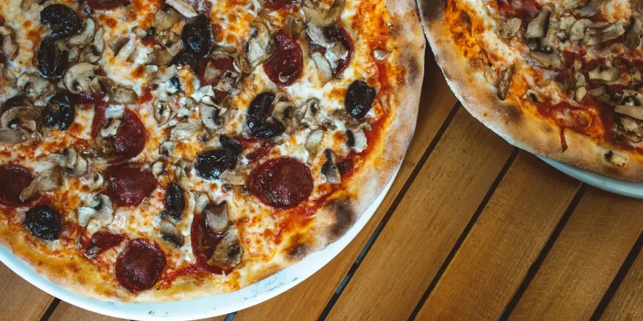 Dwie pizze z bogactwem składników na wierzchu: salami, pieczarki i czarne oliwki. Idealne na wspólny posiłek.