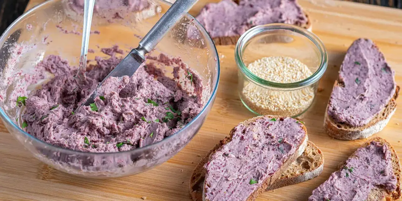 Pyszna pasta z czerwonej fasoli na chlebie, obok słoiczek sezamu. Idealna na szybką przekąskę.