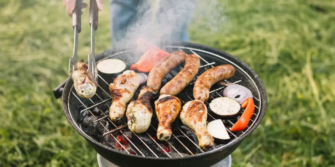 Pyszne kiełbaski i kurczak pieką się na grillu, a dym unosi się w powietrzu. Idealny sposób, jak rozpalić grilla i cieszyć się latem.
