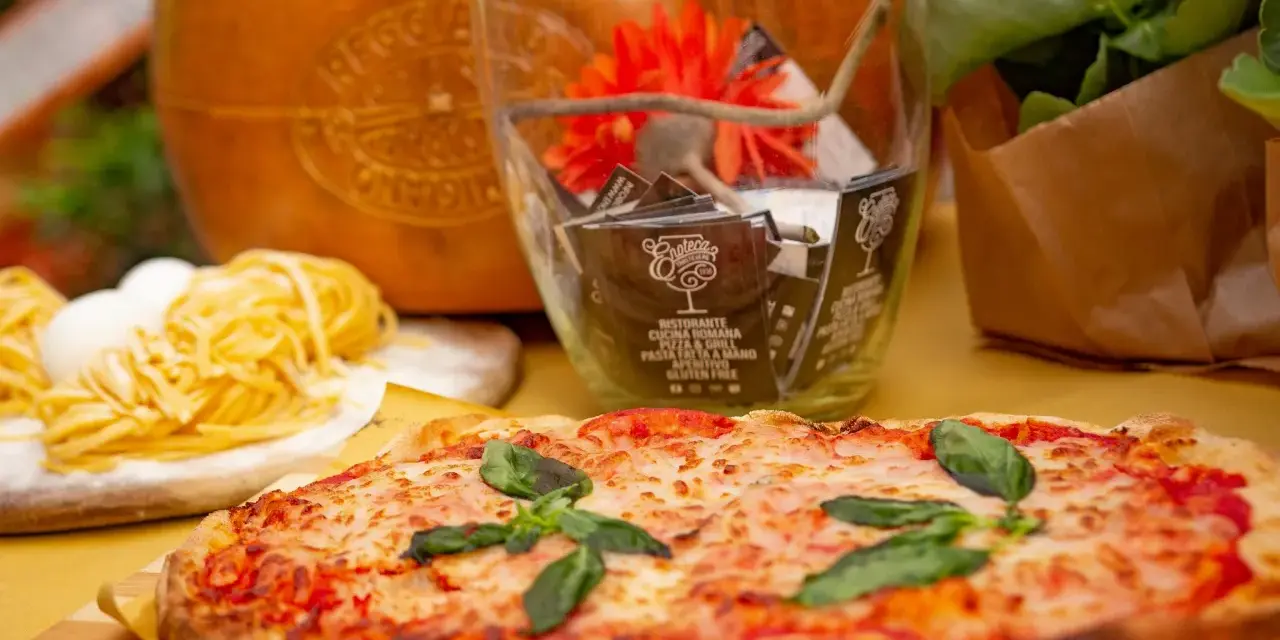 Pyszne rodzaje pizzy, makaron i ser parmezan. W tle szklany wazon z ozdobami i kwiatami.