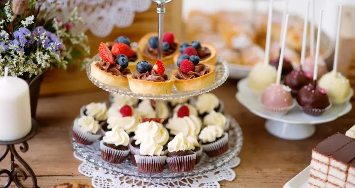 Słodkie przekąski: babeczki, tartaletki z owocami, cake pops i ciasto czekoladowe na drewnianym stole.
