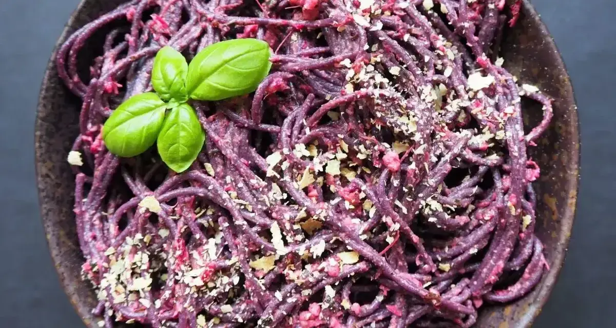 Fioletowy makaron z buraczanym pesto ze słoika, posypany orzechami i udekorowany listkiem bazylii.