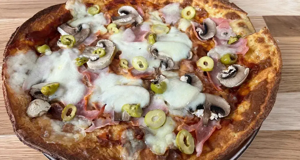 Apetyczna pizza z twarogu z pieczarkami, szynką i oliwkami, z ciągnącym się serem.