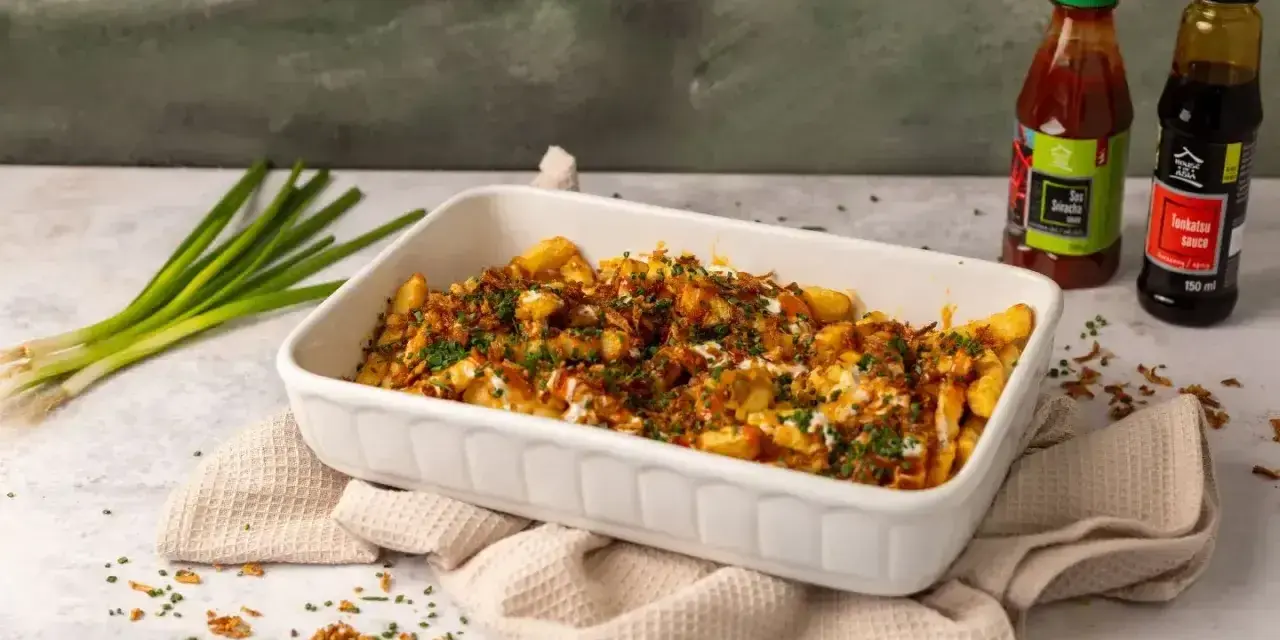 Pyszne frytki z chrupiącą posypką i sosem. Obok butelki sosu Sriracha i Tonkatsu, idealne do frytek.
