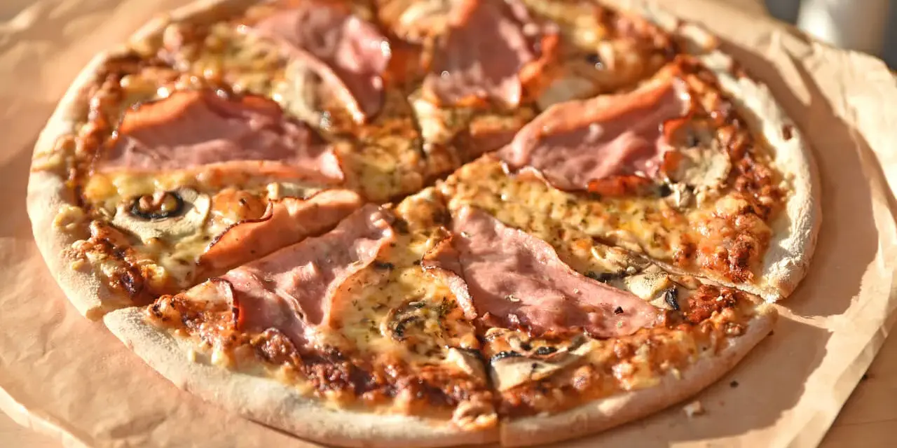 Pizza z szynką i pieczarkami, idealna na szybki obiad. Jakie pieczarki do pizzy? Te ciemne, pokrojone w plasterki, świetnie komponują się z serem i wędliną.