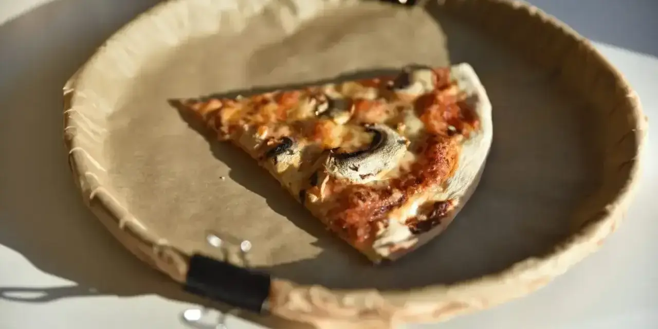 Kawałek pizzy z pieczarkami na brązowym papierze. Zastanawiasz się, ile kalorii ma pizza?
