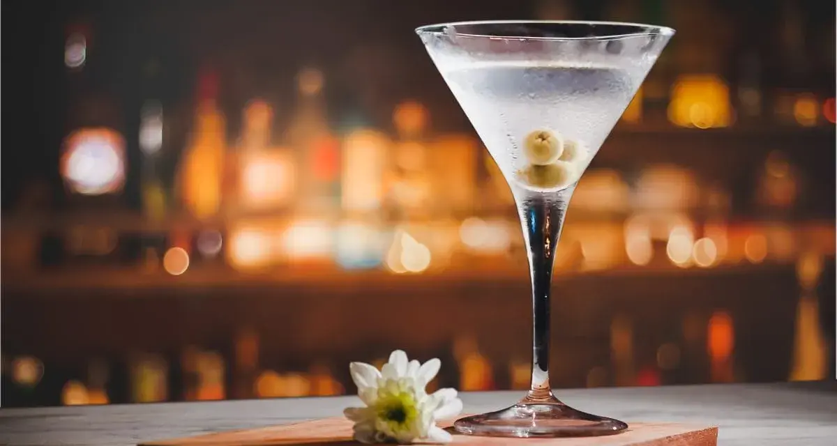 Kryształowy kieliszek z martini, trzema oliwkami i białą kwiatową ozdobą. Idealny drink, z czym pić martini?