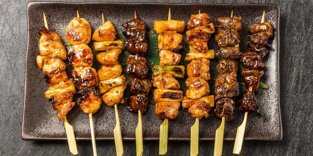 Różnorodne yakitori na talerzu: kurczak, warzywa i inne przysmaki, apetycznie wyglądające i gotowe do jedzenia.