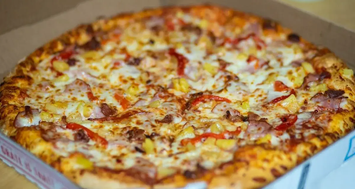 Pyszna, gorąca mrożona pizza w mikrofali, prosto z pudełka. Złocisty ser, kawałki ananasa i papryki kuszą apetycznie.