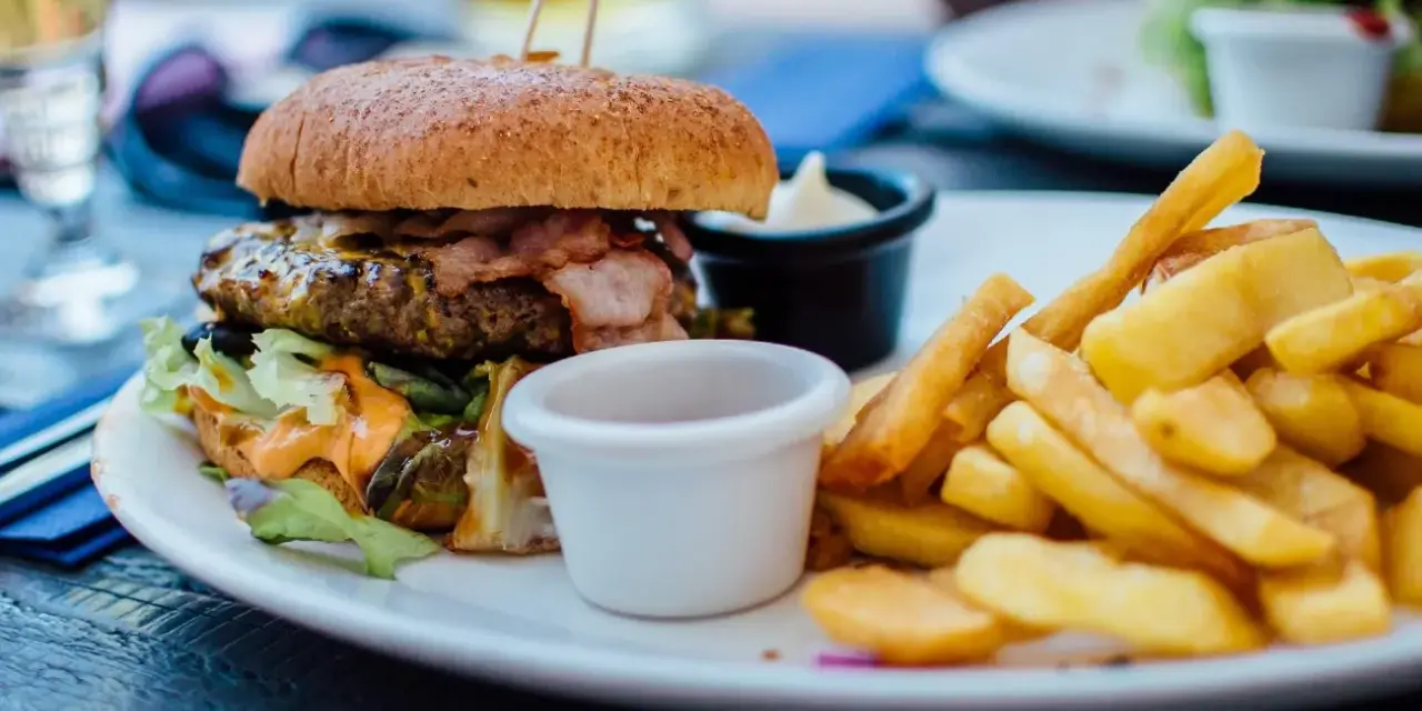 Pyszny burger z bekonem i frytki na talerzu. Idealny sposób, jak jeść burgera w restauracji, by delektować się każdym kęsem.
