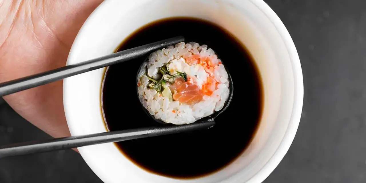 Pałeczki trzymają sushi z łososiem, zanurzając je w ciemnym sosie do sushi.